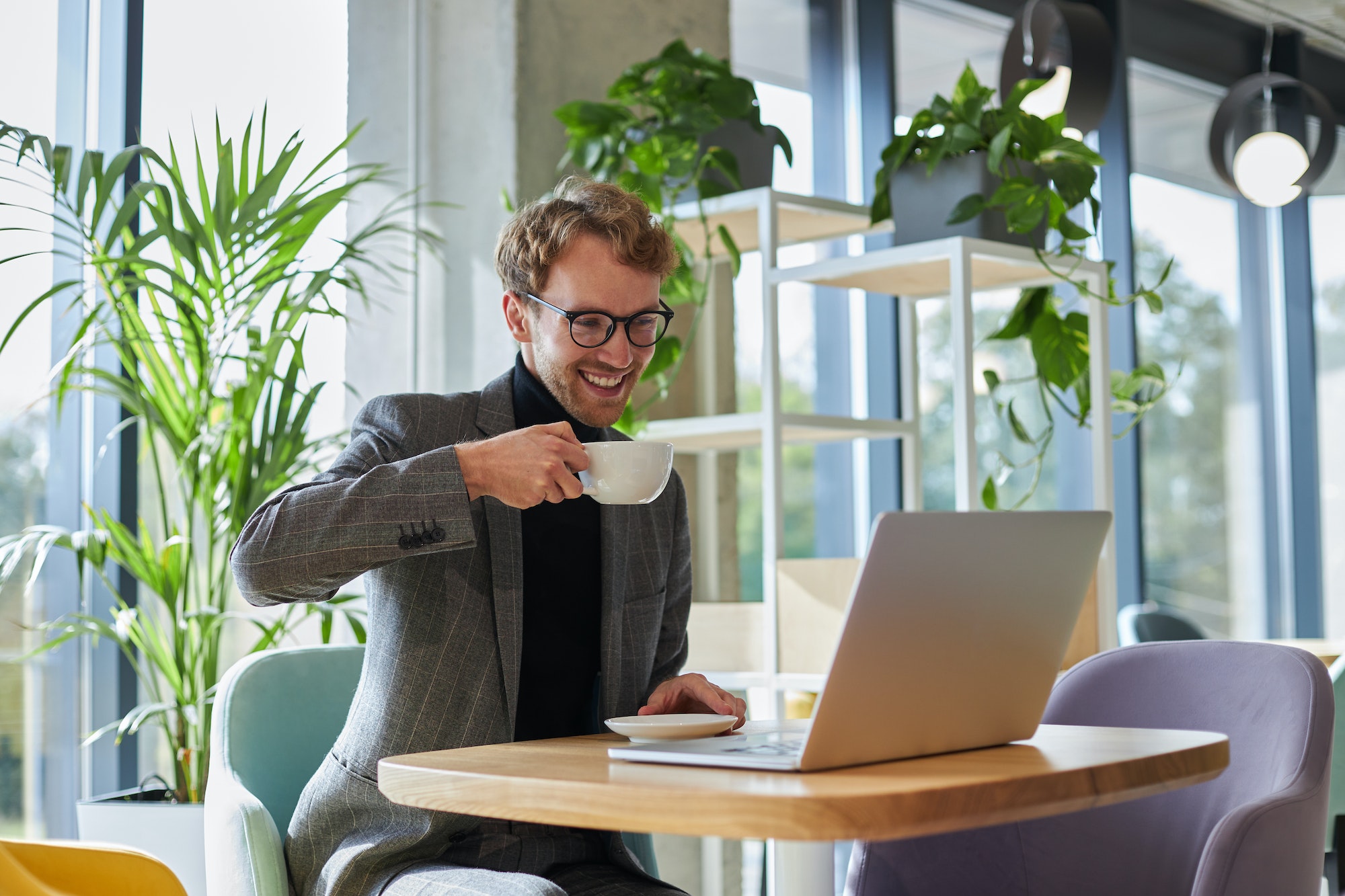 Handsome businessman in formal suit and eyeglasses, with cup of coffee while online call on laptop